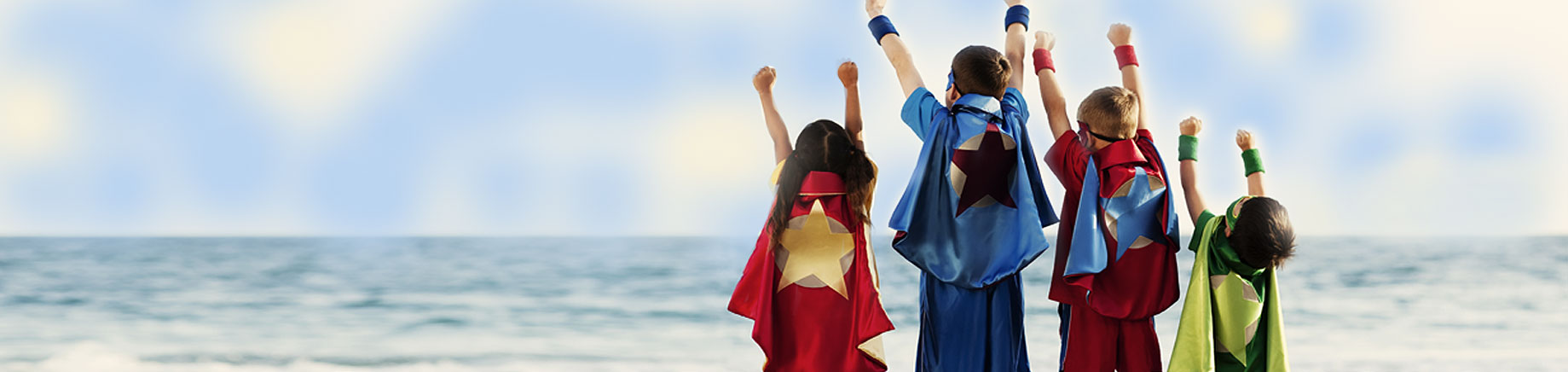 four superhero kids wearing superhero costumes looking at the ocean