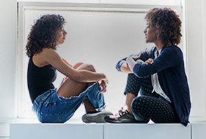 Lesbian couple sitting in window have a discussion.