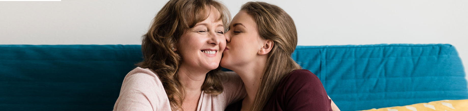 Daughter giving happy mom a kiss on the cheek.